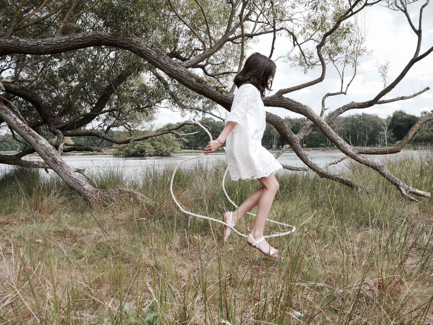 girl skipping in white dress outdoors in front of tree