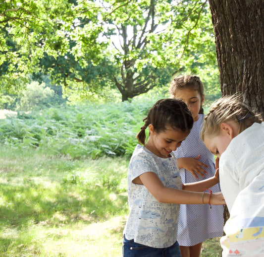 3 girls playing around base of a tree in the sunshine