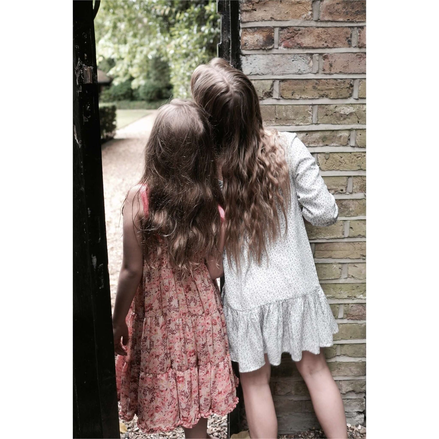 two little girls with long hair peering into a garden