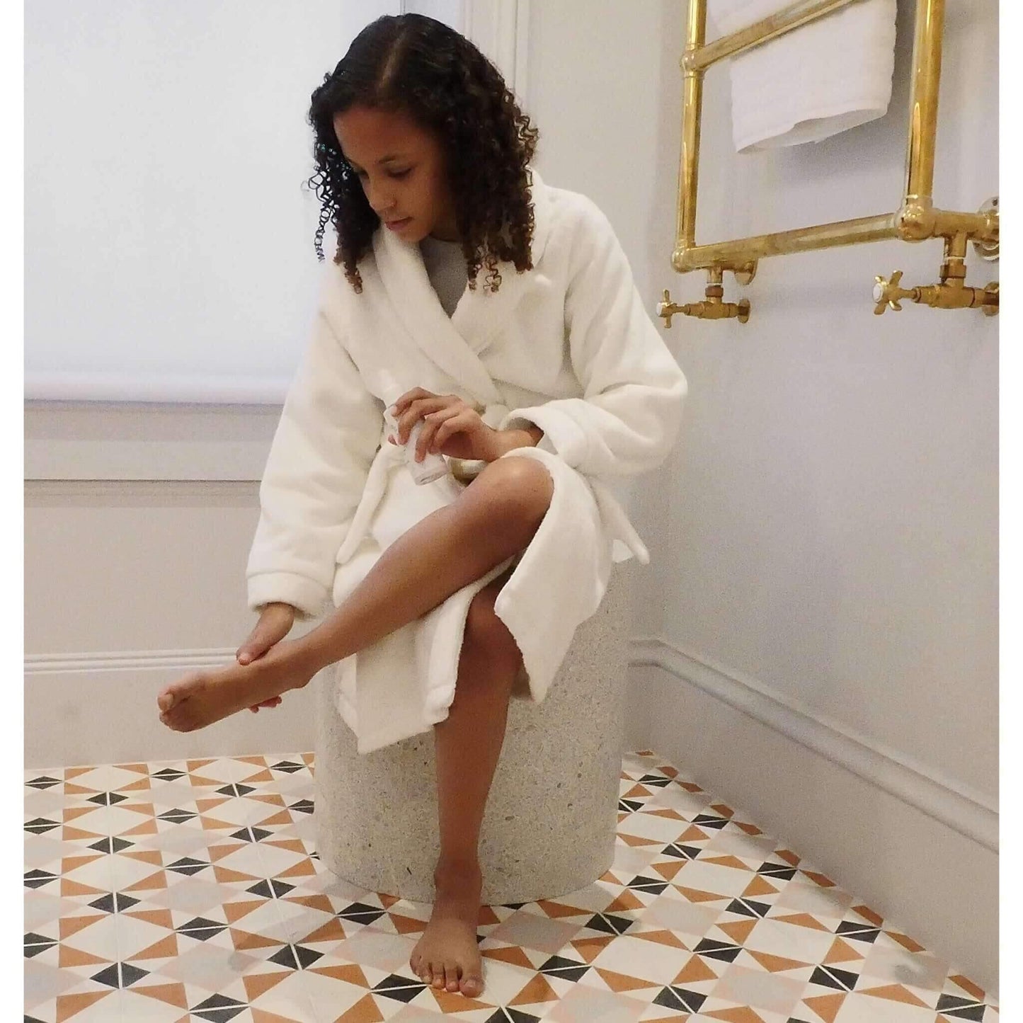 girl in white robe applying talc free lotion to feet
